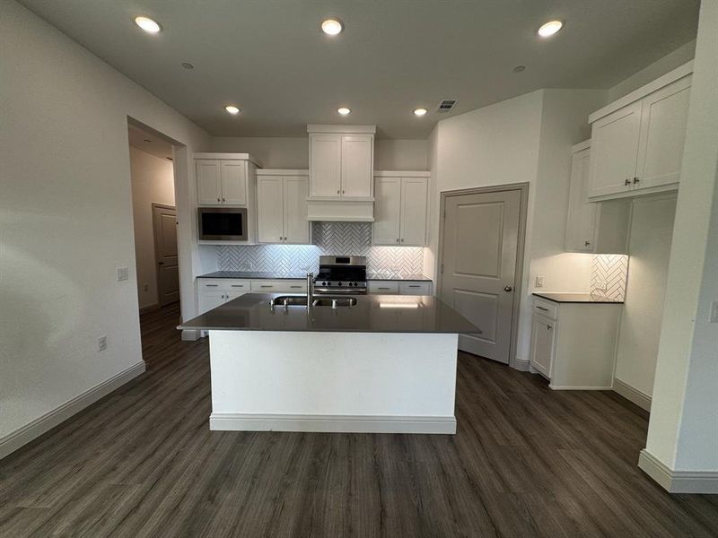 Kitchen with white cabinets, dark hardwood / wood-style floors, stainless steel appliances, and a kitchen island with sink