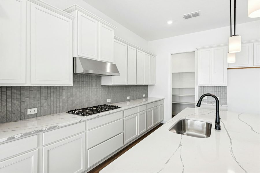 Kitchen featuring white cabinets, light stone countertops, pendant lighting, and backsplash