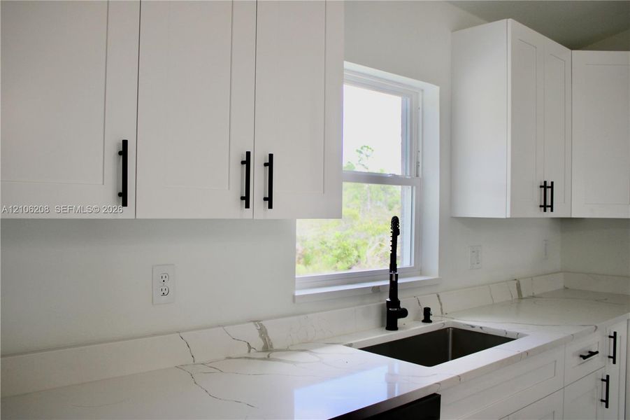 White shaker-style cabinetry with matte black pulls, light-toned stone-finish countertops with veining, under-mount stainless steel sink, and a matte black gooseneck faucet