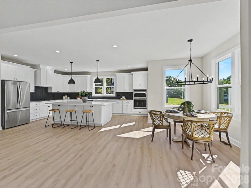 Bright designer kitchen features a large quartz island, stainless steel appliances, double ovens, abundant cabinetry, and an open-concept layout perfect for everyday living and entertaining.