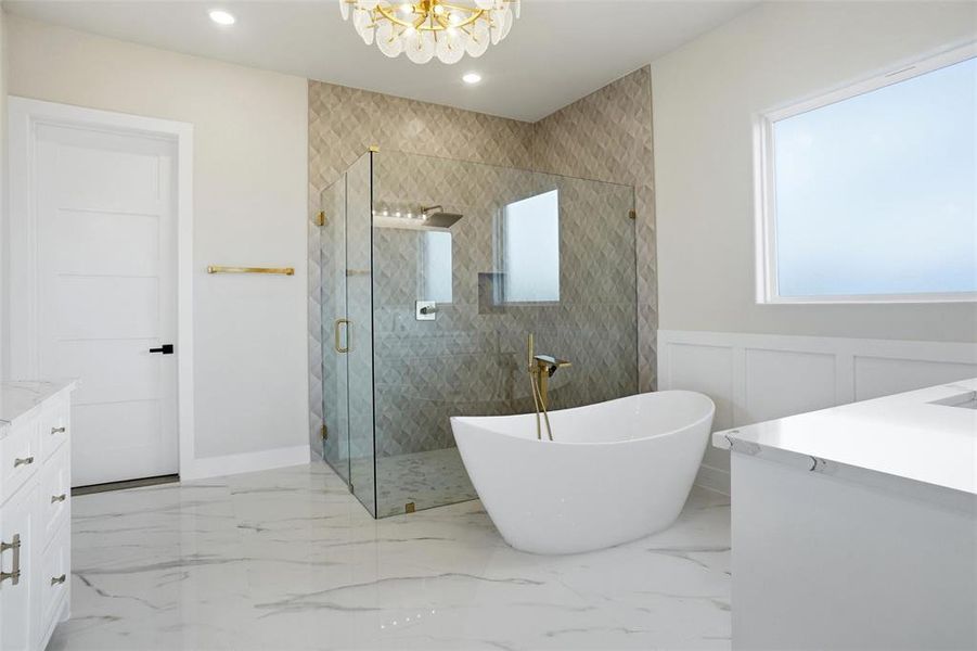 Spa-inspired primary bathroom featuring a freestanding soaking tub, walk-in glass shower, separate vanities, and access to a massive walk-in closet.