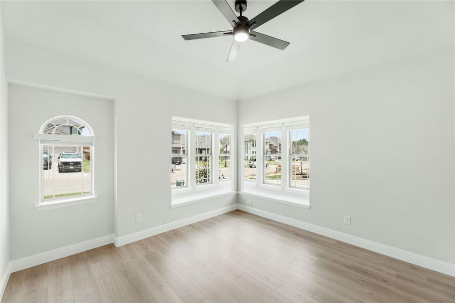 Empty room with light wood floors, ceiling fan, arched window, and corner bay windows