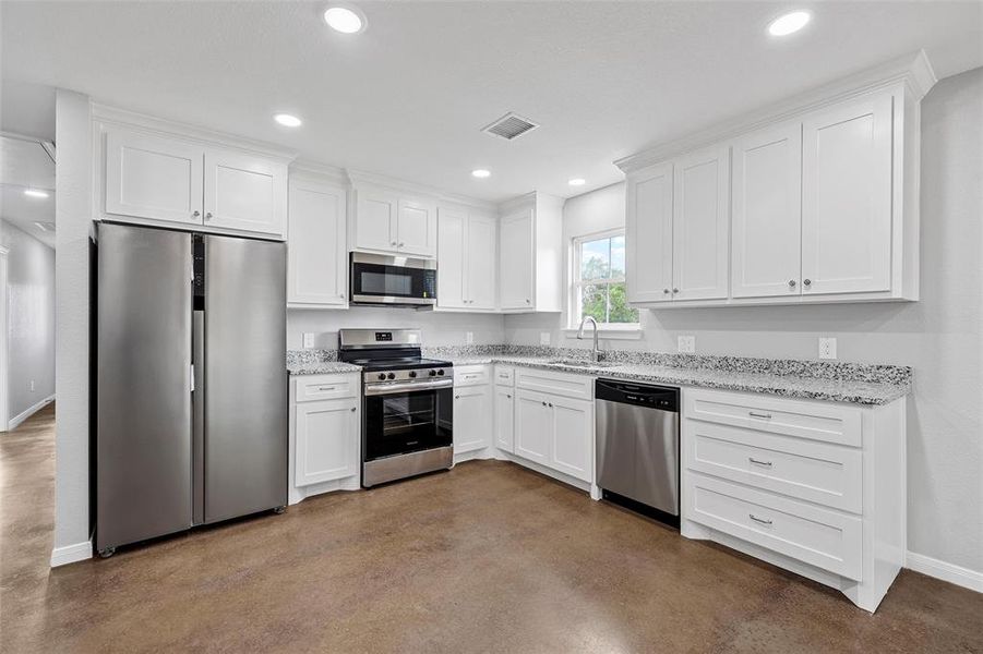 Kitchen with a sink, concrete floors, visible vents, baseboards, and appliances with stainless steel finishes