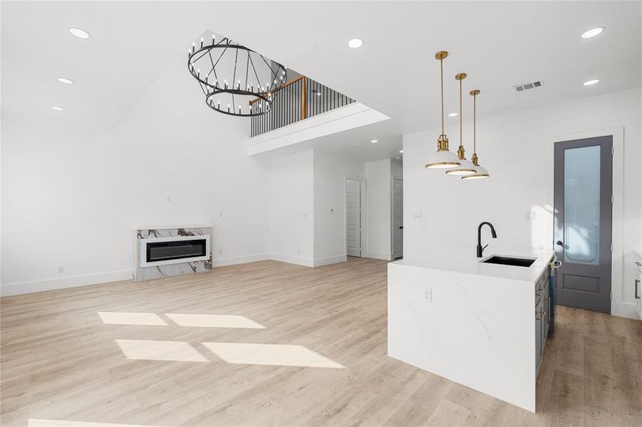 Kitchen featuring hanging lights, an island with sink, light wood-type flooring, light stone countertops, and a high ceiling Kitchen featuring hanging lights, an island with sink, light wood-type flooring, light stone countertops, and a high ceiling