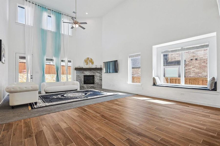 Unfurnished living room with wood-type flooring, a fireplace, a high ceiling, and ceiling fan