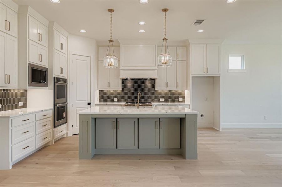 Kitchen featuring light stone countertops, white cabinetry, hanging light fixtures, a center island with sink, and backsplash Kitchen featuring light stone countertops, white cabinetry, hanging light fixtures, a center island with sink, and backsplash