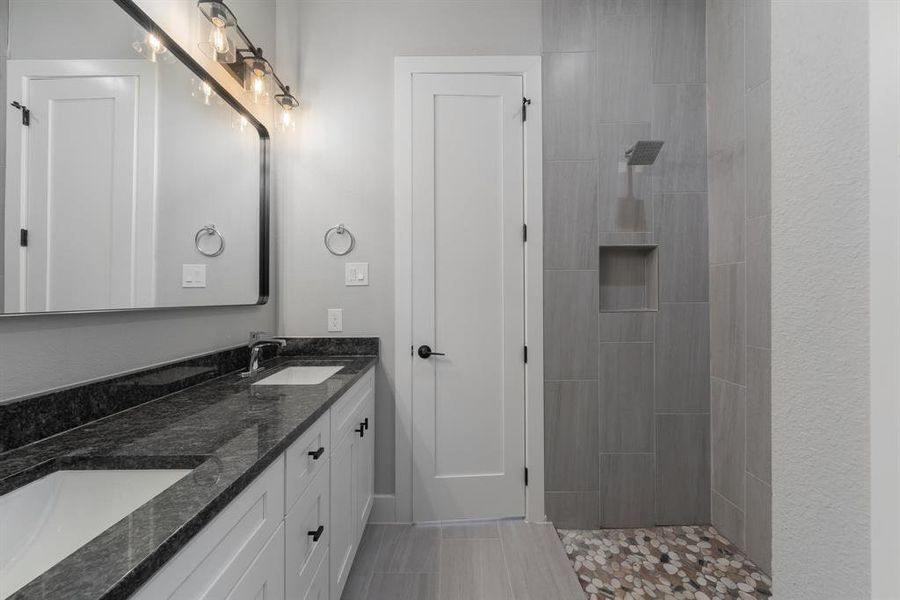 Full bath with a sink, double vanity, and a tile shower