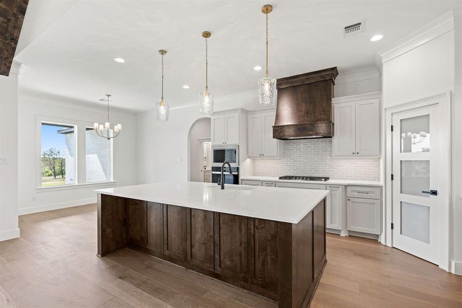 Kitchen featuring built in microwave, decorative backsplash, arched walkways, custom range hood, and visible vents