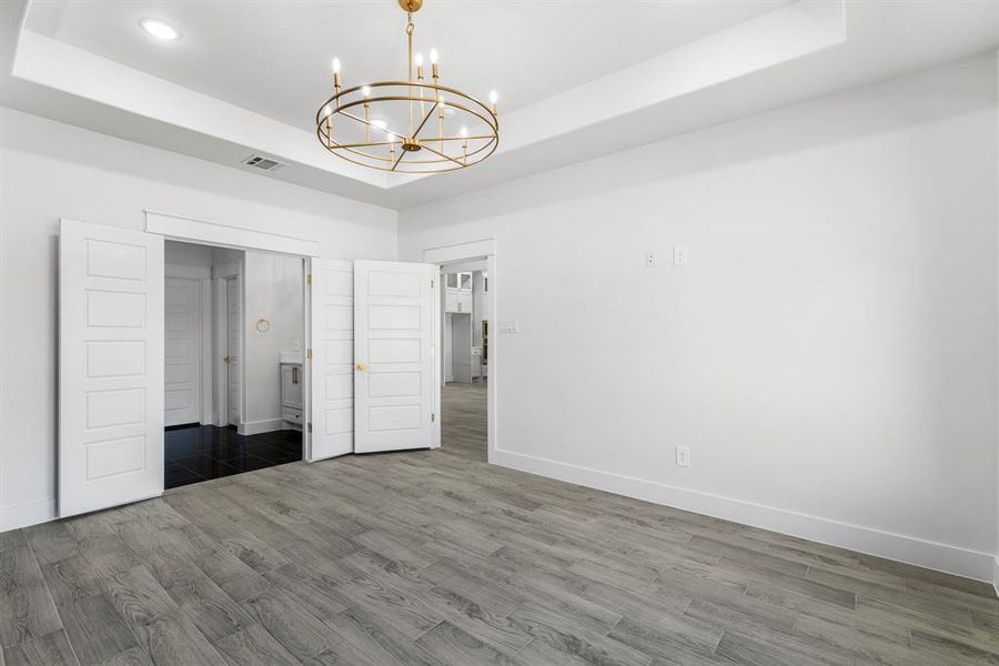 Unfurnished bedroom featuring a closet, a raised ceiling, dark wood-type flooring, and an inviting chandelier