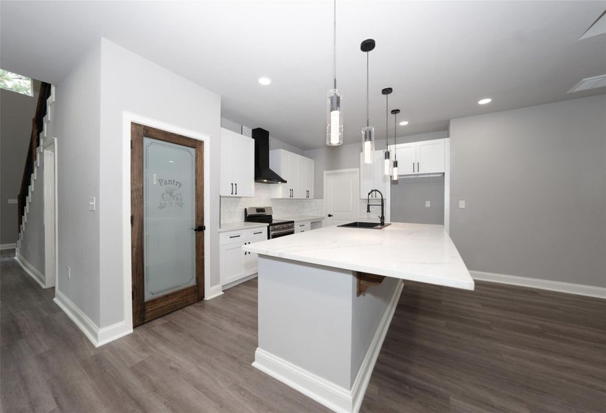 This spacious open-concept kitchen and living area features modern finishes, including sleek pendant lighting, a large island with a sink, and stylish cabinetry. The room is well-lit with recessed lighting and natural light from multiple windows, complemented by light wood floors and a ceiling fan.