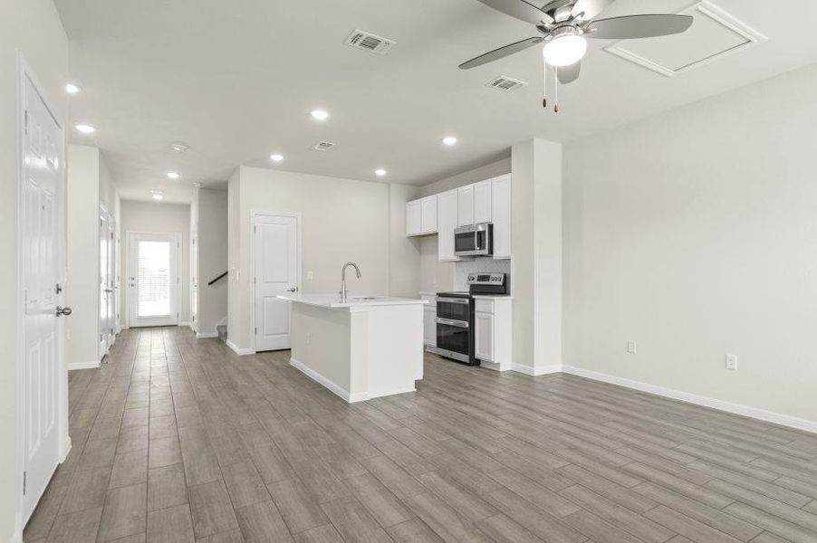 Kitchen featuring an island with sink, stainless steel appliances, white cabinetry, ceiling fan, and open floor plan