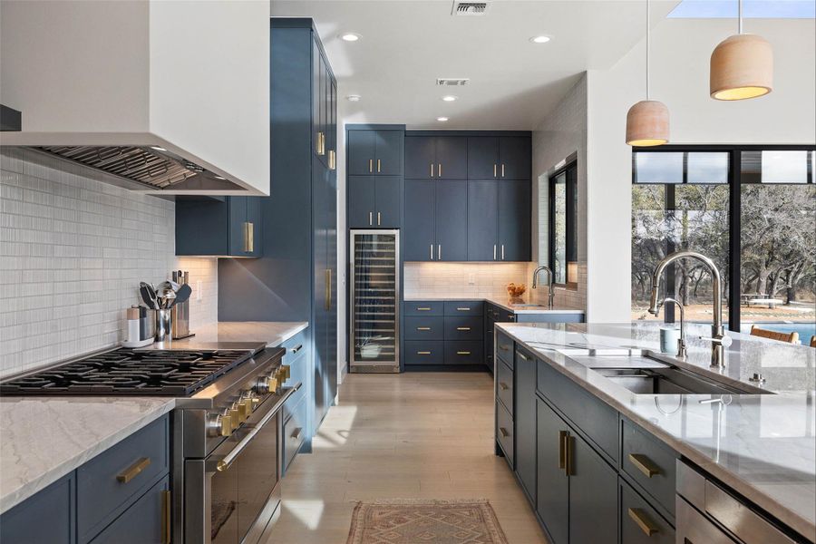 Kitchen featuring double oven range, decorative light fixtures, wall chimney exhaust hood, light stone countertops, and beverage cooler