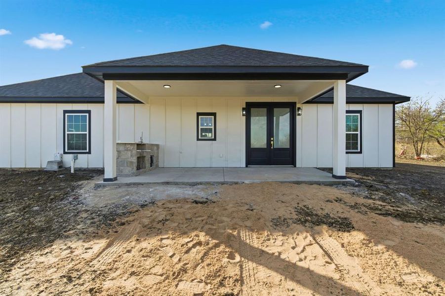 Rear view of property featuring a shingled roof, board and batten siding, french doors, and a patio