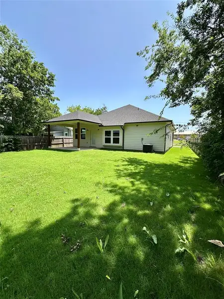 Expansive green lawn with a covered patio, featuring wood support columns and a dark shingle roof Expansive green lawn with a covered patio, featuring wood support columns and a dark shingle roof