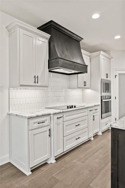 Kitchen with white cabinets, tasteful backsplash, recessed lighting, light stone counters, and custom range hood
