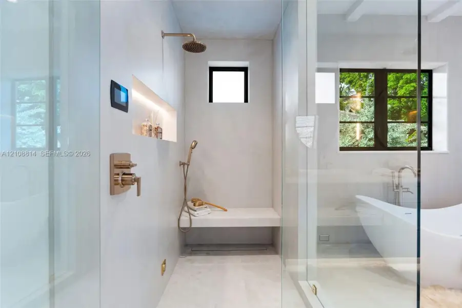 Walk-in shower featuring a built-in stone bench, rain showerhead with handheld sprayer, recessed shelving with integrated lighting, digital control interface, and floor-to-ceiling glass enclosure Walk-in shower featuring a built-in stone bench, rain showerhead with handheld sprayer, recessed shelving with integrated lighting, digital control interface, and floor-to-ceiling glass enclosure