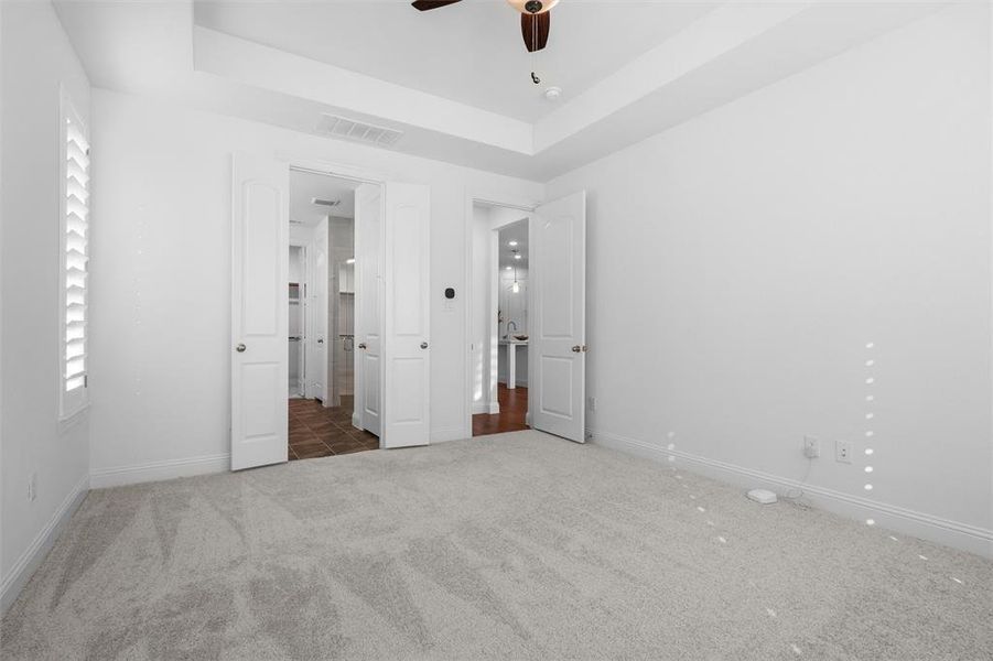 Unfurnished bedroom with ceiling fan, a raised ceiling, and carpet