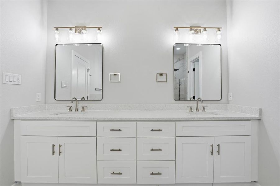 Dual vanity featuring white shaker-style cabinetry, light speckled countertops, rectangular framed mirrors, and brushed nickel hardware and fixtures