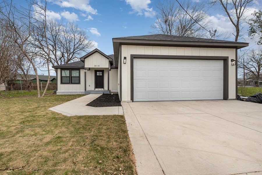 View of front facade featuring a front lawn, fence, concrete driveway, an attached garage, and a shingled roof