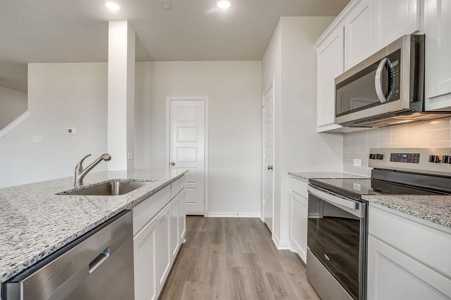 Kitchen featuring appliances with stainless steel finishes, white cabinetry, light stone counters, light wood-type flooring, and recessed lighting