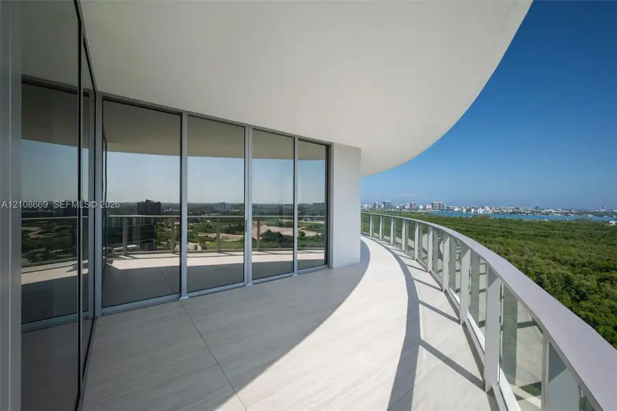 Curved balcony featuring light-toned tile flooring, glass panel railing, floor-to-ceiling sliding glass doors, and a deep overhang