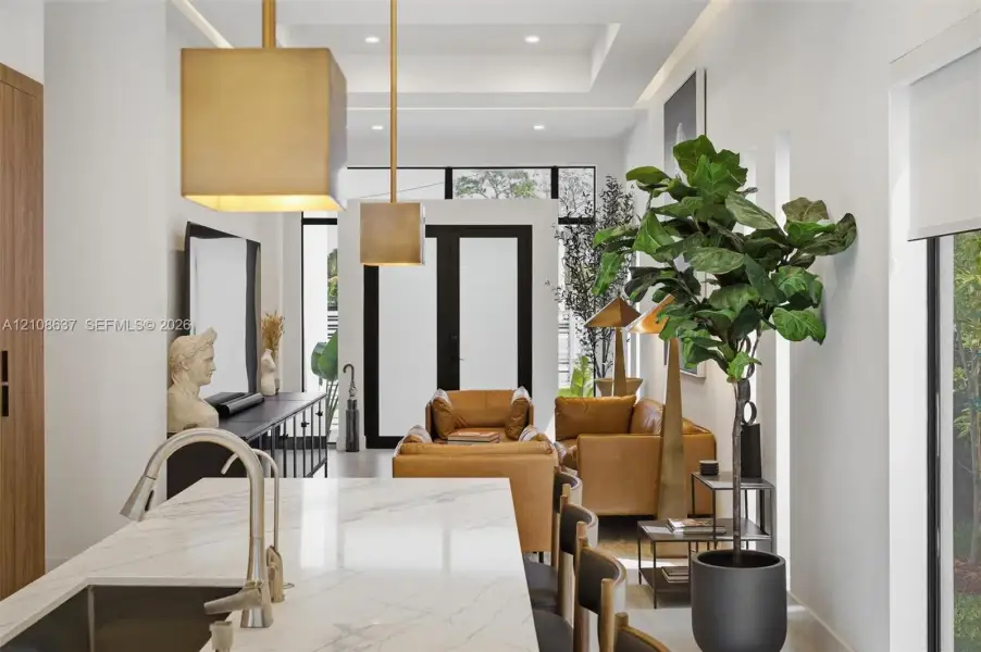 Kitchen featuring a stone-surface island with a stainless steel undermount sink and polished faucet, complemented by recessed tray ceiling lighting and suspended metallic pendant fixtures