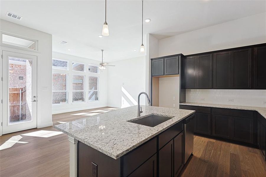 Kitchen featuring backsplash, a center island with sink, sink, hardwood / wood-style flooring, and light stone counters