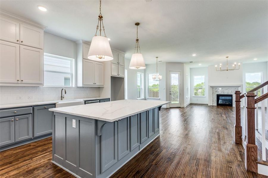 Kitchen with gray cabinets, dark wood-type flooring, hanging light fixtures, and a premium fireplace