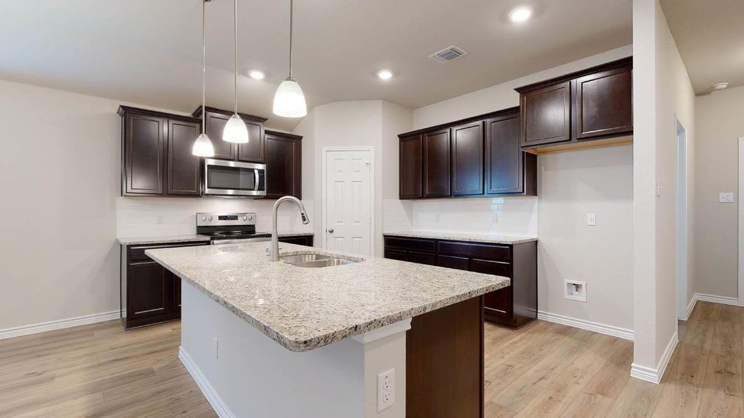 Kitchen featuring dark wood finish cabinetry, light stone counters, hanging light fixtures, stainless steel appliances, and light wood-style flooring