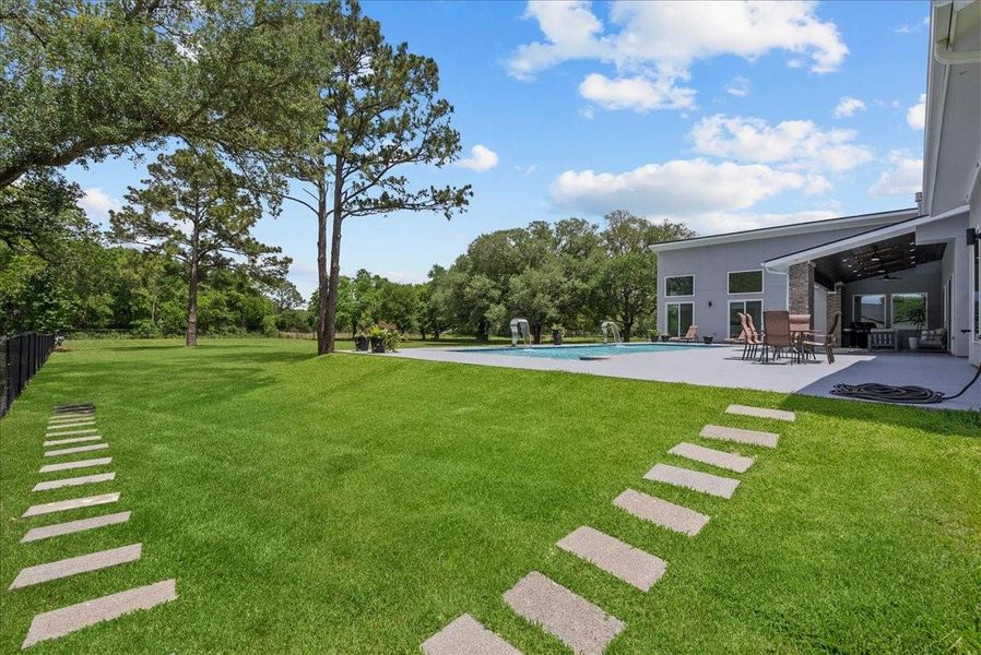 Modern stepping stones lead across a sprawling, lush lawn toward the resort-style pool and terrace.