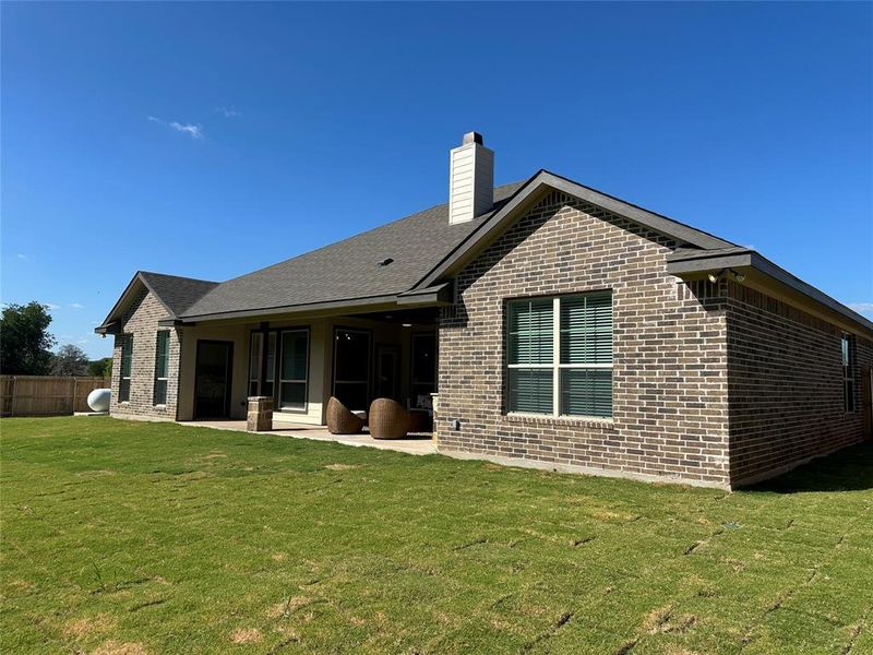 Exterior featuring brick and stucco siding, a covered patio, a gabled roof, a prominent chimney, and a landscaped lawn