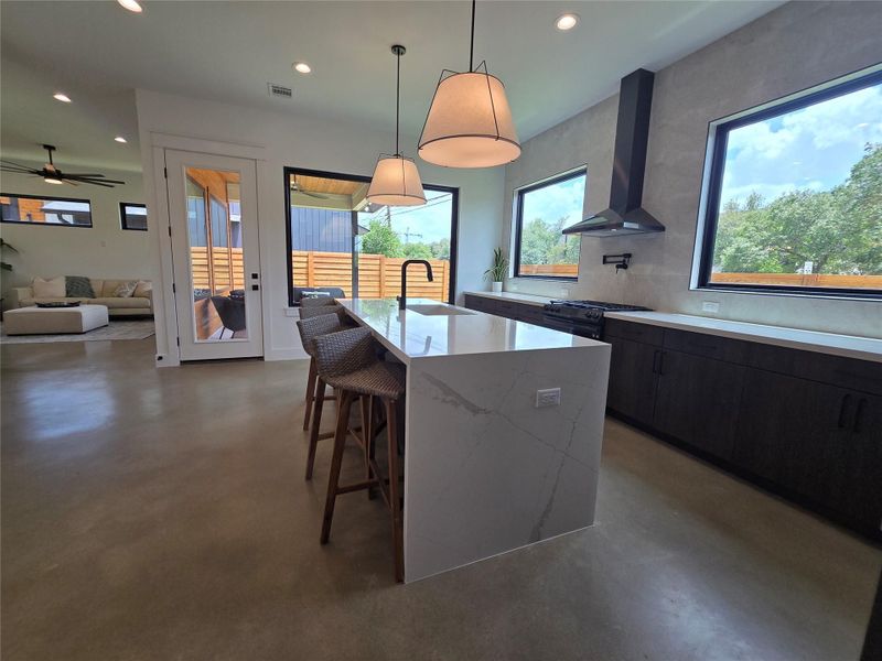 Kitchen with wall chimney exhaust hood, concrete floors, recessed lighting, a breakfast bar area, and a kitchen island with sink