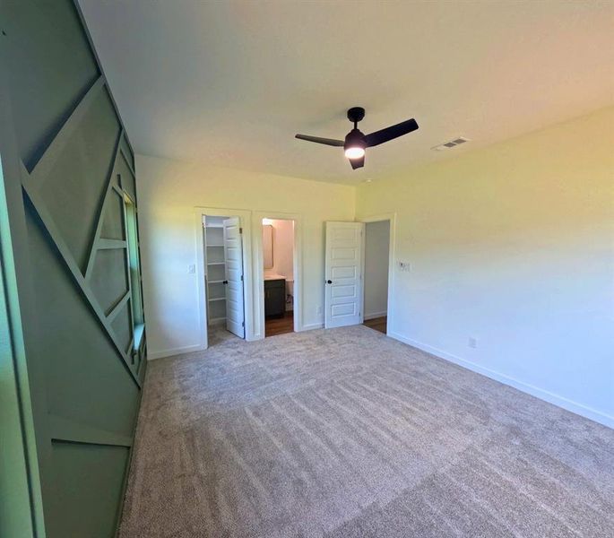 Unfurnished bedroom with ensuite bathroom, a walk in closet, carpet floors, and ceiling fan Unfurnished bedroom with ensuite bathroom, a walk in closet, carpet floors, and ceiling fan