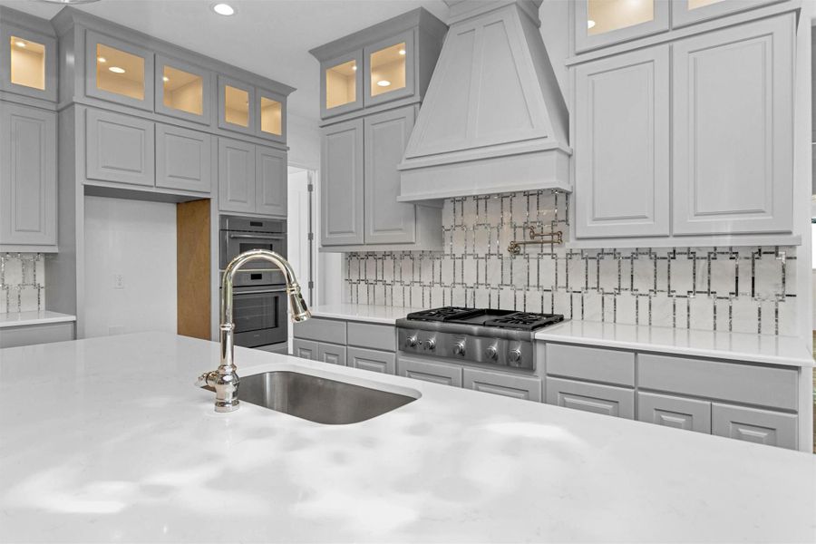 Crafted for the culinary enthusiast, this kitchen showcases a premium gas cooktop with pot filler, quartz counters, stainless steel oven and microwave, and soft-lit display cabinetry for a sleek, functional finish. Crafted for the culinary enthusiast, this kitchen showcases a premium gas cooktop with pot filler, quartz counters, stainless steel oven and microwave, and soft-lit display cabinetry for a sleek, functional finish.