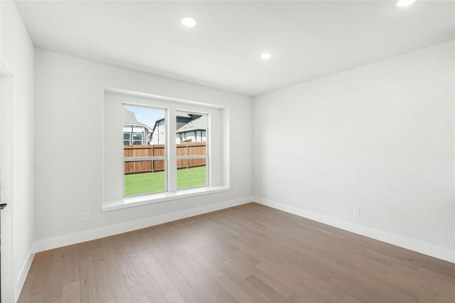 Empty room with white walls, hardwood floors, recessed lighting, and a window overlooking a fenced backyard Empty room with white walls, hardwood floors, recessed lighting, and a window overlooking a fenced backyard