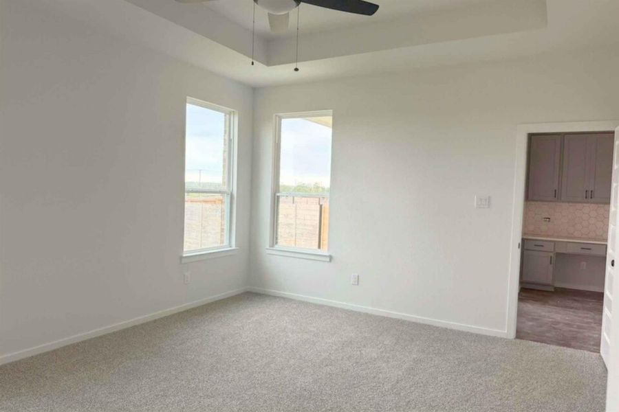 Carpeted spare room featuring a tray ceiling and ceiling fan