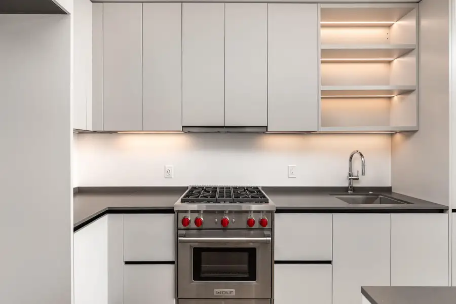 Kitchen showcasing sleek cabinetry, illuminated shelving, and high-end stainless steel appliances.