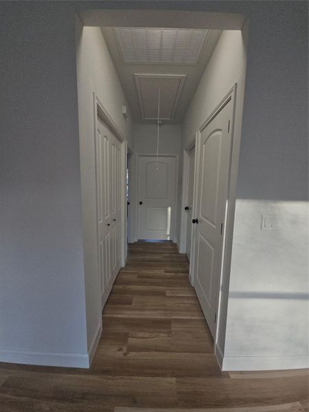 Hallway featuring attic access, wood finished floors, baseboards, and visible vents