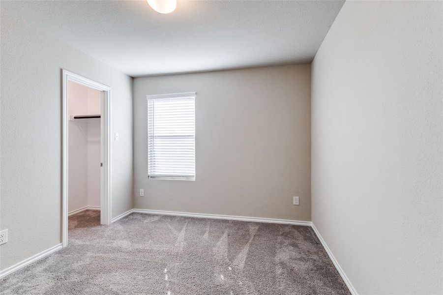 Unfurnished bedroom with light colored carpet, a walk in closet, and a closet