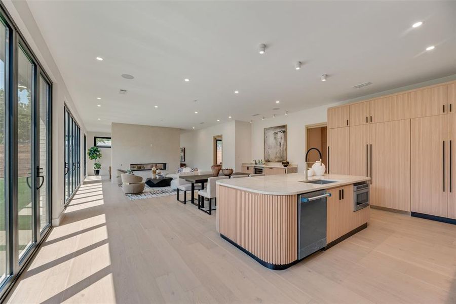 Kitchen featuring light wood-type flooring, light brown cabinets, dishwasher, a kitchen island with sink, and sink