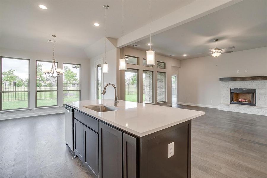 Kitchen with hardwood / wood-style floors, ceiling fan with notable chandelier, sink, an island with sink, and a stone fireplace