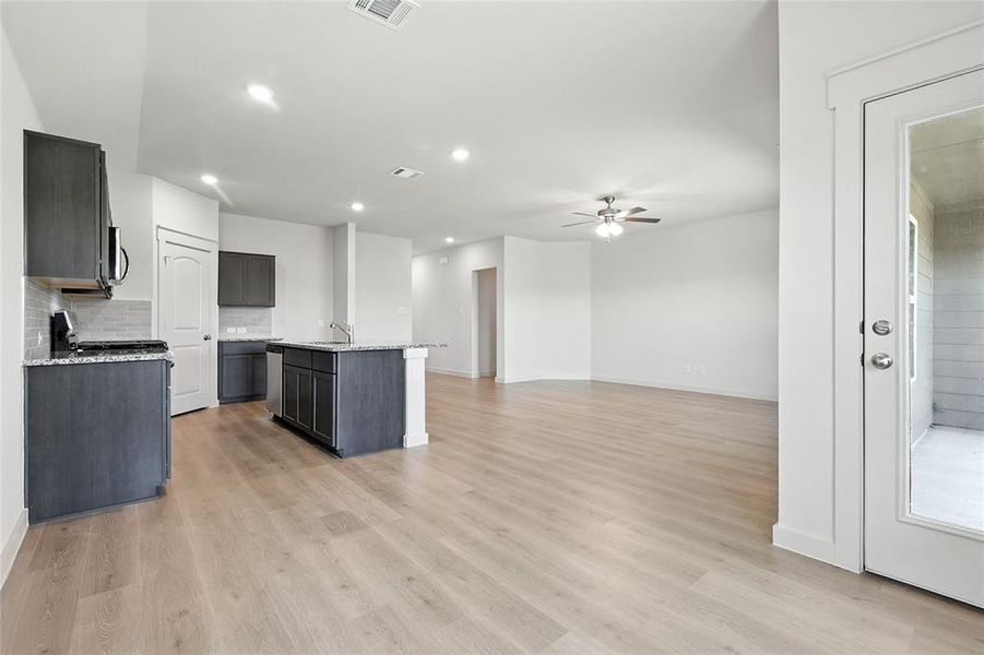 Kitchen with a kitchen island with sink, light stone countertops, open floor plan, backsplash, and recessed lighting Kitchen with a kitchen island with sink, light stone countertops, open floor plan, backsplash, and recessed lighting