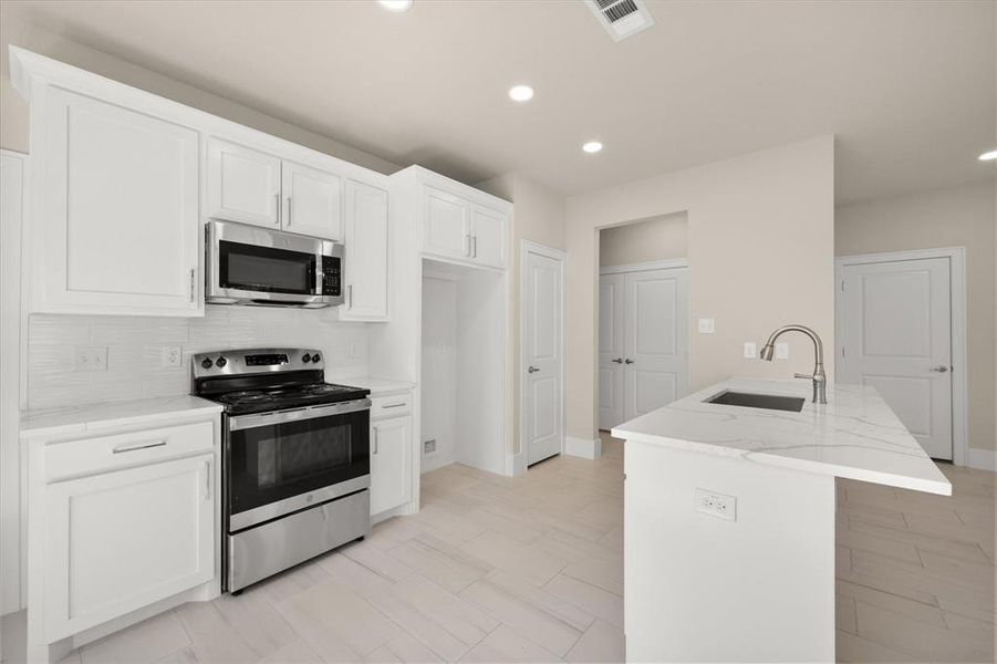 Kitchen with appliances with stainless steel finishes, sink, light stone counters, backsplash, and white cabinetry