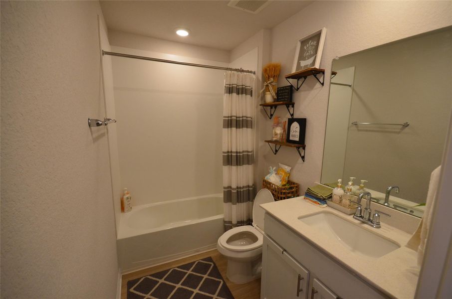 Bathroom featuring vanity, shower / bath combination with curtain, recessed lighting, wood finished floors, and a textured wall Bathroom featuring vanity, shower / bath combination with curtain, recessed lighting, wood finished floors, and a textured wall