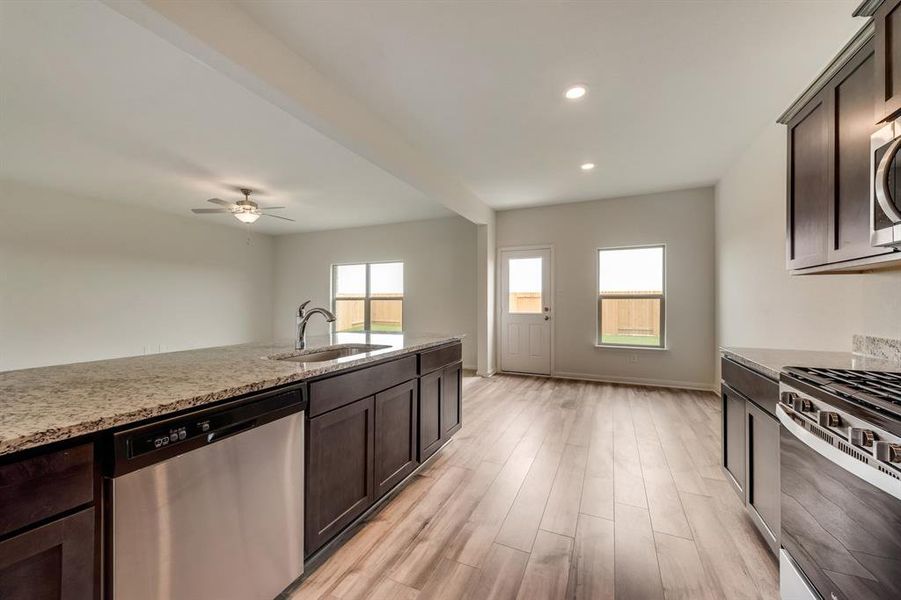 Kitchen with light stone countertops, sink, light wood-type flooring, and appliances with stainless steel finishes