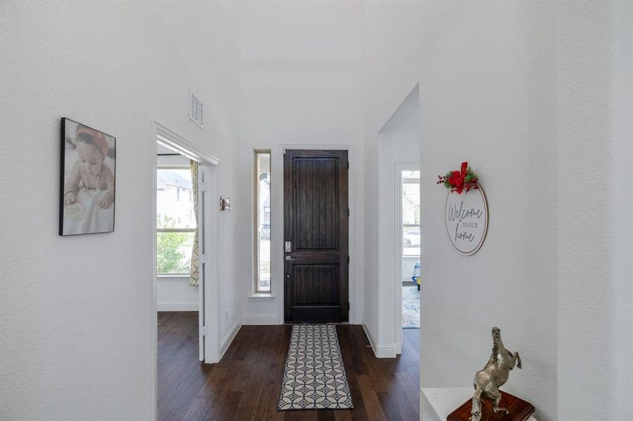 Foyer featuring dark wood-type flooring, a high ceiling, visible vents, and baseboards