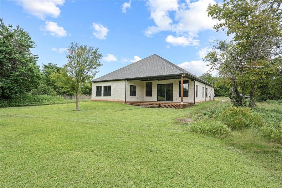 Back of house with brick siding, a lawn, a shingled roof, and ceiling fan