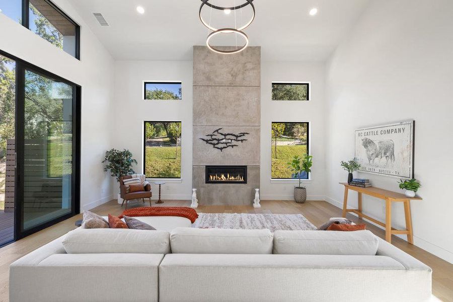 The great room centers around a designer wall mounted fireplace flanked by stacked windows for natural light and serene hill country views.