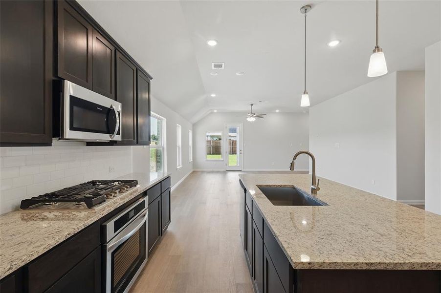 Kitchen with stainless steel appliances, a sink, lofted ceiling, light wood finished floors, and backsplash