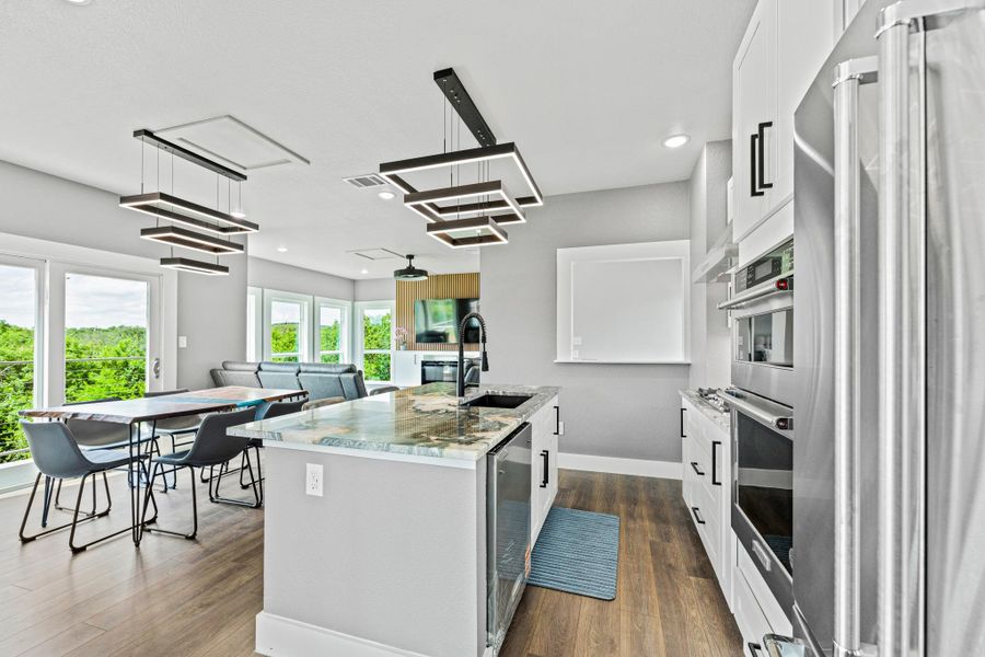 Open-concept kitchen and dining area featuring a kitchen island with sink, white cabinetry, stainless steel appliances, and wood-finish flooring